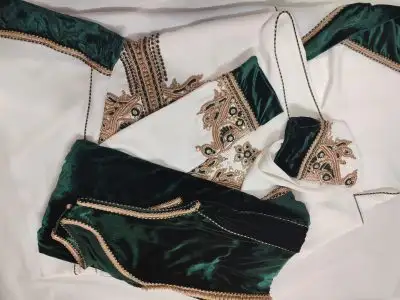 Caftan En Ligne Découvrez l'élégance intemporelle du caftan henna, une pièce traditionnelle marocaine magnifiquement ornée. Nos caftans en henna allient beauté et tradition pour des moments inoubliables. Explorez notre collection unique aujourd'hui ! Le caftan safaa, composé de deux pièces en crêpe de soie blanc, travaillé en zewak maalam, sfifa et button en skali bronze. Le bas est confectionné en velours de soie vert royal, Il est accompagné d'une ceinture assortie.